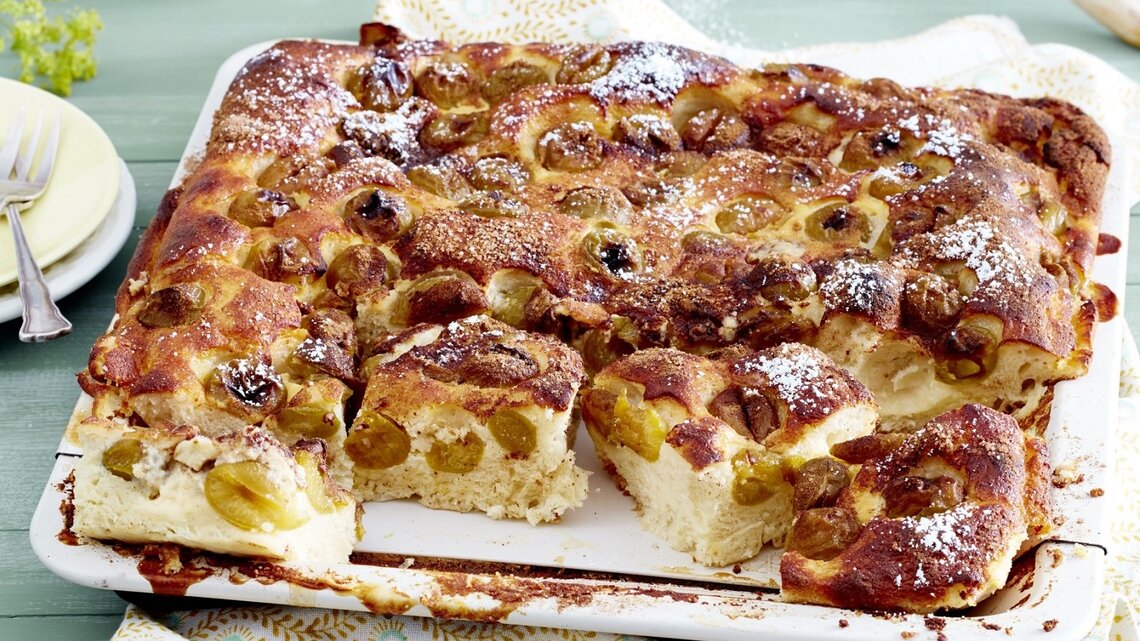 Auf einem Backblech liegt ein Mirabellen-Blechkuchen. Er ist mit Puderzucker bestreut. 