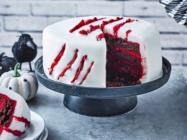 Diese gruselige Halloween-Torte ist einfach zubereitet und ist ein richtiger Hingucker für Ihre Halloween-Party! Auf einem Tortenteller steht eine gruselige Halloween-Torte. Sie ist mit weißem Fondant eingedeckt und hat blutige Risse als Dekoration.