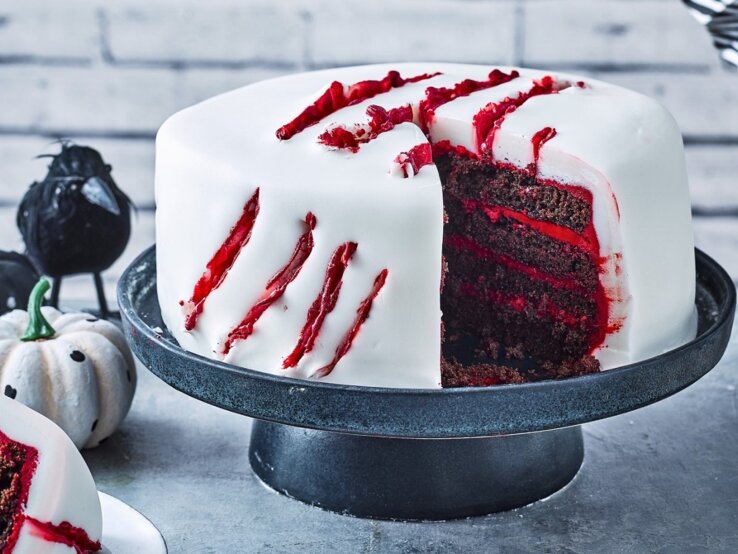 Diese gruselige Halloween-Torte ist einfach zubereitet und ist ein richtiger Hingucker für Ihre Halloween-Party! Auf einem Tortenteller steht eine gruselige Halloween-Torte. Sie ist mit weißem Fondant eingedeckt und hat blutige Risse als Dekoration.