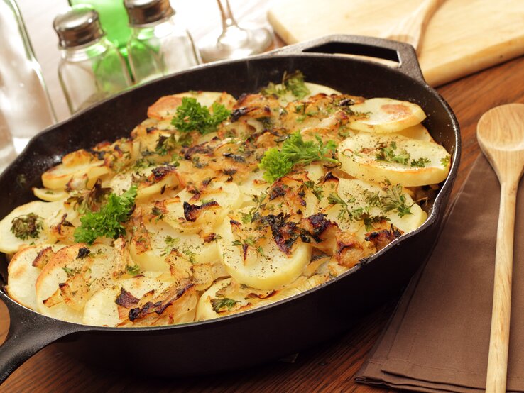 Kartoffeln Lyonnaise in gusseiserner Pfanne auf Holz. 