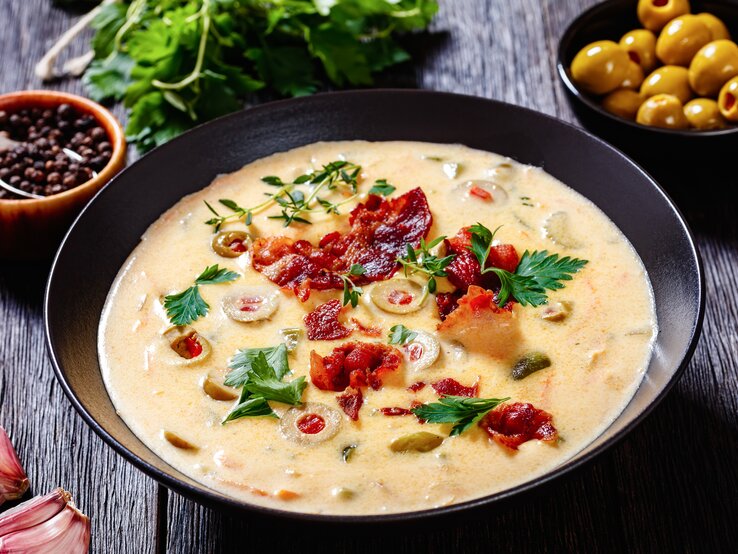 Unsere Käse-Bier-Suppe wird im Nu zu Ihrem liebsten Herbst-Gericht. Käse-Bier-Suppe mit Bacon in schwarzer Schale auf schwarzem Holz.