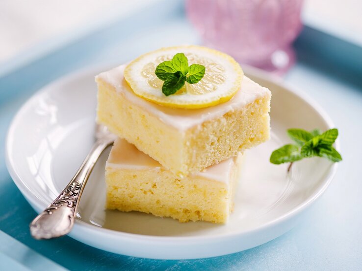 Zwei quadratische Stücke Zitronenkuchen auf einem weißen Teller. 