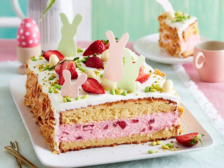 Auf einer Kuchenplatte ist eine Erdbeer-Ostertorte serviert. Sie ist mit Erdbeeren und Osterhasen aus Esspapier dekoriert.