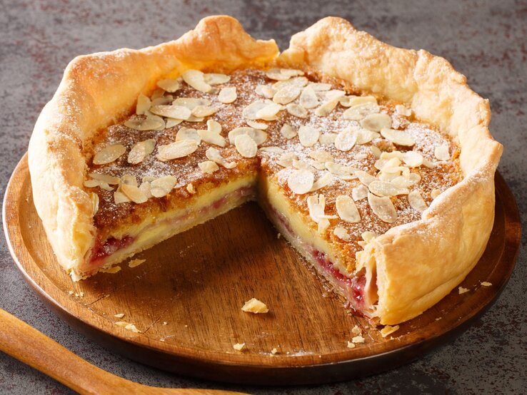 Ein Bakewell-Pudding auf einem Holzbrett auf einem grauem Steintisch.