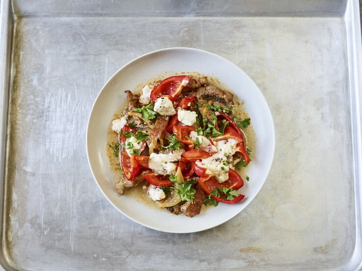 Ofen-Gyros mit Paprika und Feta vom Blech in einem tiefen Teller. Dieser steht auf einem Blech. 