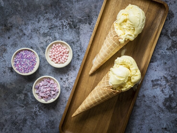 Eiscreme in Waffeln auf einem kleinen Holzbrett mit bunten Zuckerperlen auf einem dunklen Steintisch.