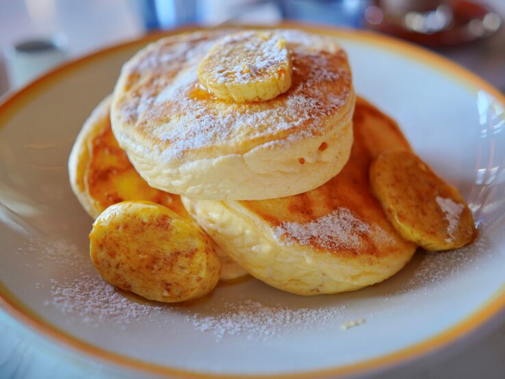 Drei japanische Pancakes mit einigen kartamellisierten Bananenscheiben in einem tiefen hellen Teller auf einem Marmoruntergrund.