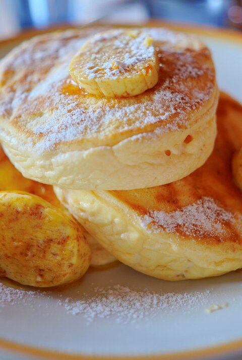 Drei japanische Pancakes mit einigen kartamellisierten Bananenscheiben in einem tiefen hellen Teller auf einem Marmoruntergrund.