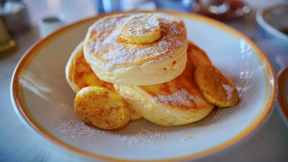 Drei japanische Pancakes mit einigen kartamellisierten Bananenscheiben in einem tiefen hellen Teller auf einem Marmoruntergrund.