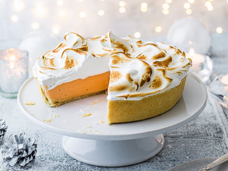 Ein angeschnittener Negroni-Pie mit goldbraun gebräuntem Baiser steht auf einer weißen Tortenplatte.