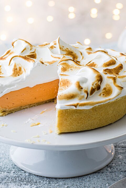 Ein angeschnittener Negroni-Pie mit goldbraun gebräuntem Baiser steht auf einer weißen Tortenplatte.