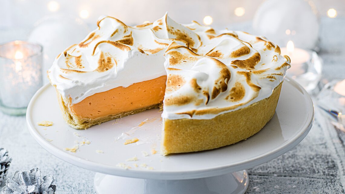 Ein angeschnittener Negroni-Pie mit goldbraun gebräuntem Baiser steht auf einer weißen Tortenplatte.