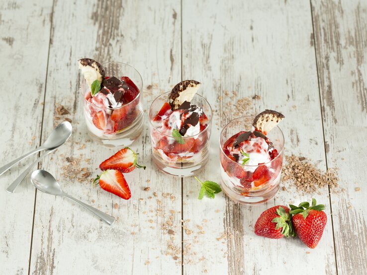 Drei Schalen mit Schokokuss-Erdbeer-Dessert auf weißem Holzuntergrund. 