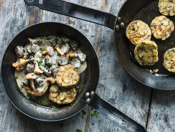 Feinste Sterneküche: Ein bayerisches Pilzragout mit Brezenknödeln! Auf einem Teller ist eine Portion bayerisches Pilzragout mit Brezenknödeln angerichtet. Daneben steht eine Pfanne mit weiteren Knödeln.