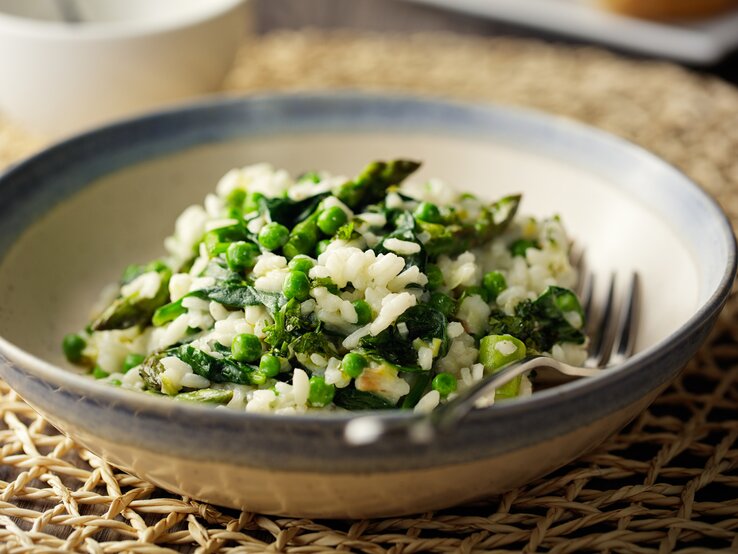 Ein Teller veganes Spargelrisotto mit Erbsen und Spinat, darin liegt eine Gabel.