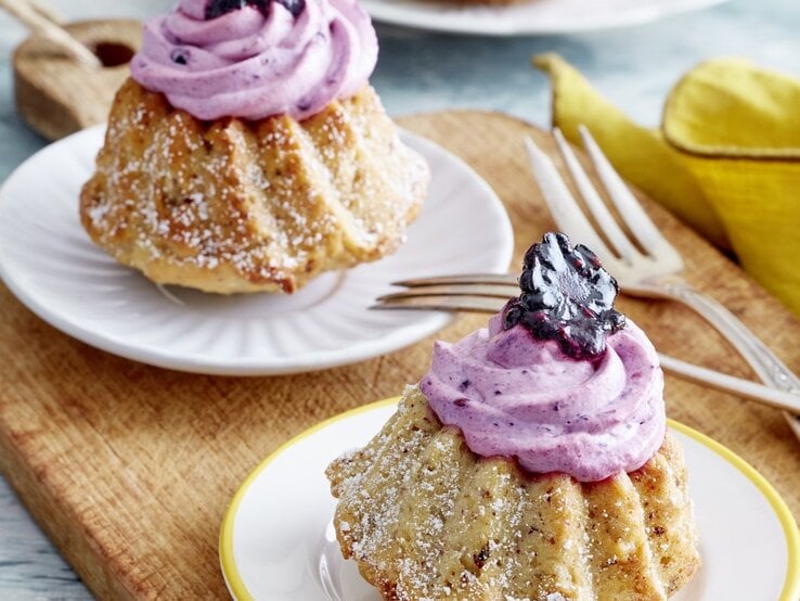 Auf zwei Tellern stehen je ein Apfelmus-Mini-Gugelhupf. Sie sind mit einer Creme und Brombeeren verziert. 