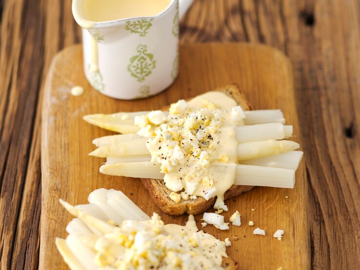 Toast mit Spargel und Eier-Soße auf Holzbrett serviert.