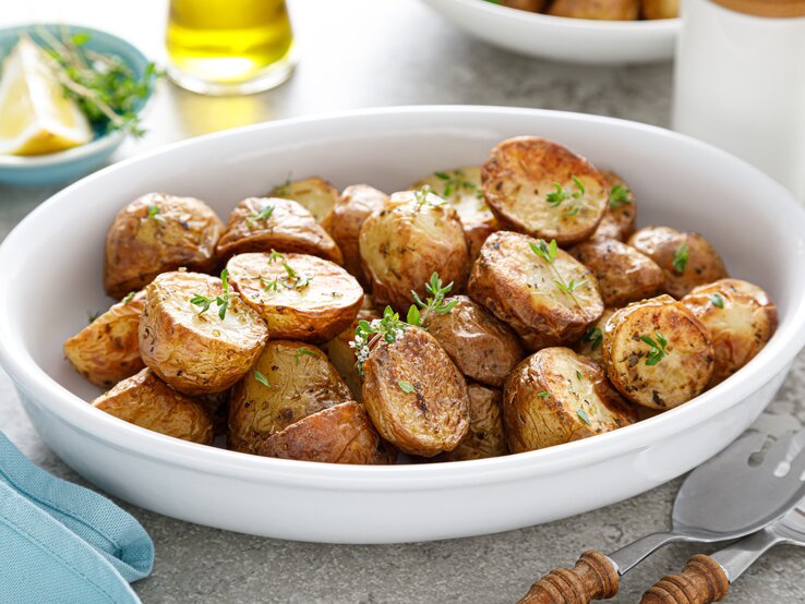 Eine weiße Schüssel mit gebackenen Kartoffeln und Thymian. 