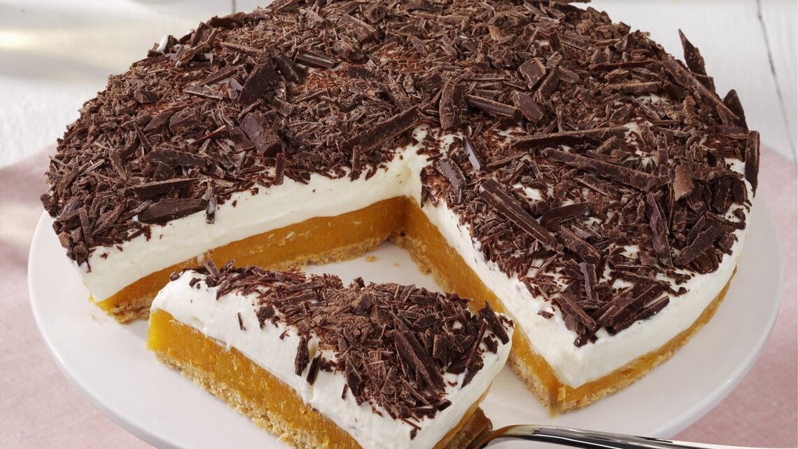 Auf einem Teller liegt eine Aprikosen-Joghurt-Torte ohne Backen. Sie ist mit Schokoraspeln bestreut.