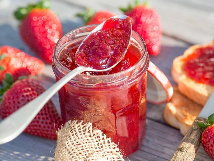 Ein Glas Erdbeer-Aperol-Marmelade ist mit Löffel, Erdbeeren und Toast.