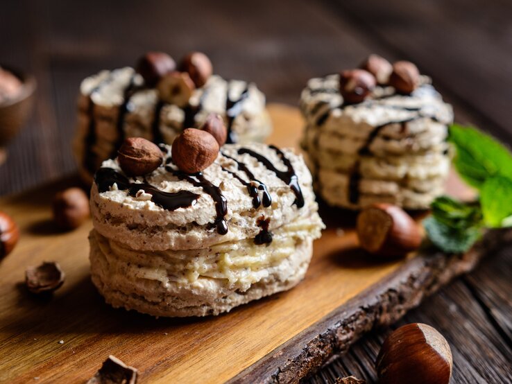 Haselnuss Baiser mit Creme auf einem Holzbrett mit Nüssen, Minze und Schokolade verziert.
