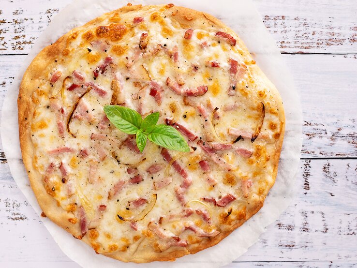 Carbonara-Pizza auf hellem, hölzernem Untergrund. 