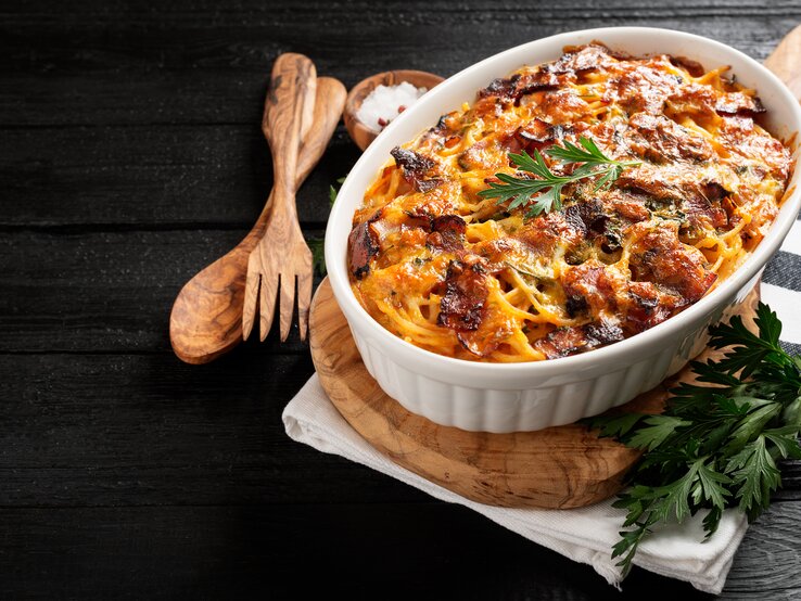 Spaghetti-Auflauf mit Hähnchen in einer weißen Auflaufform.  Daneben steht eine Schüssel mit Meersalz und Holzbesteck. 