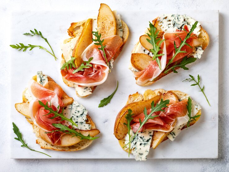 Fingerfood-Klassiker: Crostini mit Birne, Schinken und Gorgonzola Crostini mit Birne, Schinken und Gorgonzola auf einer grauen Keramik-Platte.