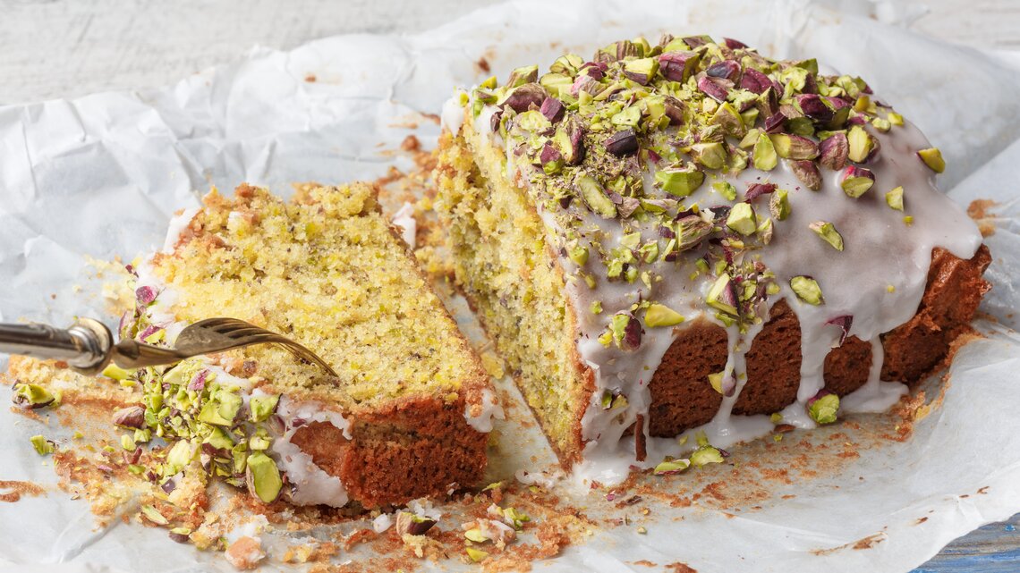 Ein angeschnittener Pistazien-Zitronenkuchen aus der Kastenform.