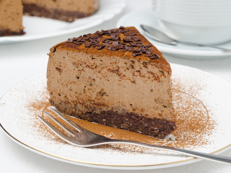 Ein Stück veganer Schokoladen-Cheesecake mit Kakao und Schokosplittern bestreut auf einem kleinen Teller.