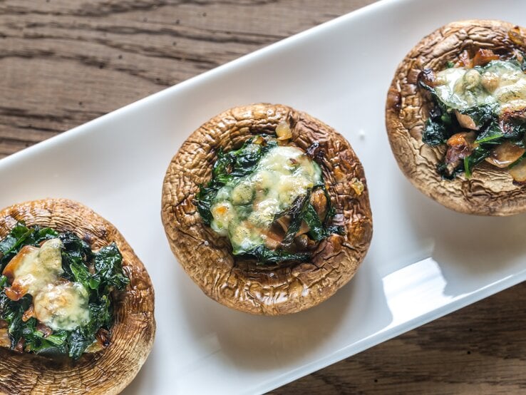 Draufsicht auf drei mit Spinat und Käse gefüllte Champignons. 