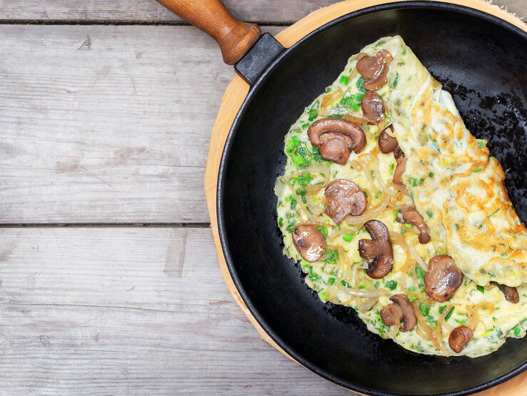 Eine Pfanne mit dem Pilz-Omelette auf einem hellen Holztisch direkt von oben fotografiert.