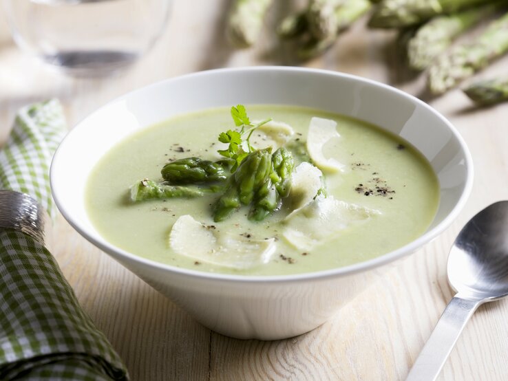 Spargelcremesuppe mit Parmesan in weißer Schale garniert mit Spargelköpfen. 