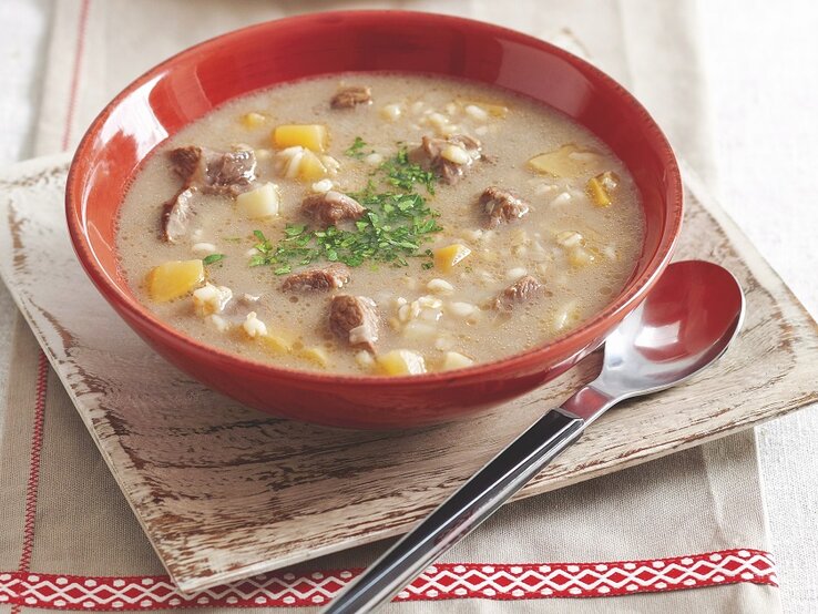 Graupensuppe in rundem Teller / Löffel / Untergrund Holzschlale auf Tisch 