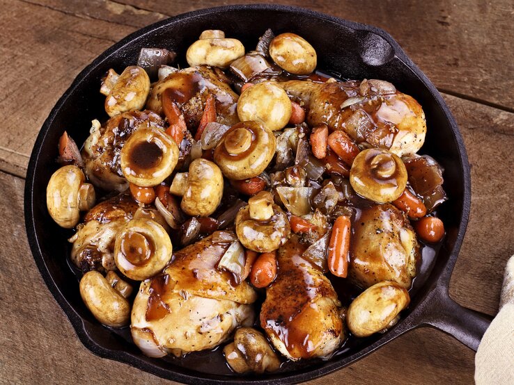 Gusseiserne Pfanne auf Holz gefüllt mit Coq au vin samt Pilze und Fleisch. 