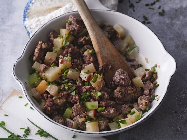 Hackfleischpfanne mit Gemüse und Schinken / runde Schüssel mit Holzlöffel / Draufsicht, schräg
