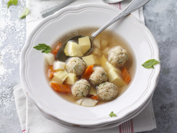 Ein weißer Teller mit der Rindfleischsuppe auf grauem Untergrund direkt von oben fotografiert.