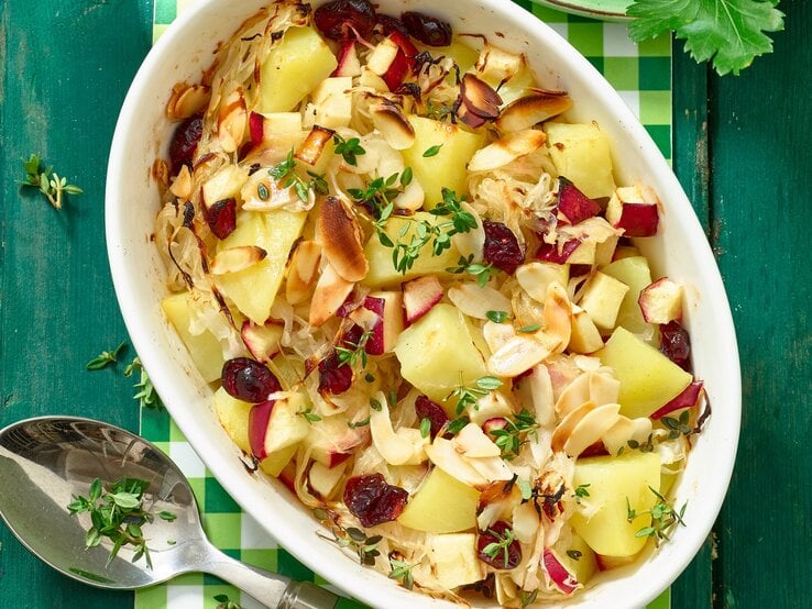 Kartoffel-Sauerkraut-Auflauf in einer ovalen Schüssel von oben fotografiert. Unten auf dem Foto ein Löffel, oben Petersilie.