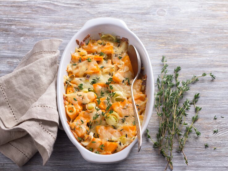 Kürbisgratin_mit_Lauch Draufsicht auf eine weiße Auflaufform. in ihr: ein schlotziger Kürbisauflauf überbacken mit Käse und würzigem Thymian. Das ganze steht auf einem hellen Holztisch.