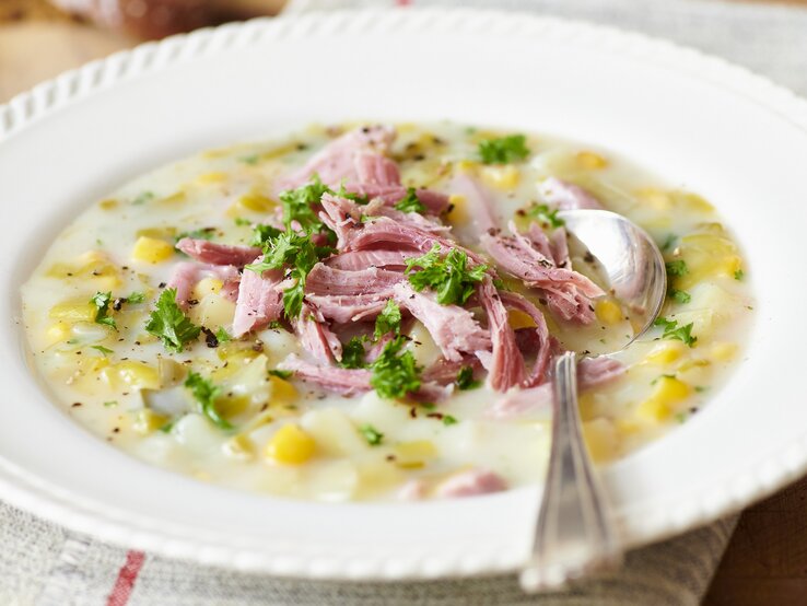 Runder verzierter Teller mit einer Lauch-Mais-Suppe, garniert mit Schinken. 