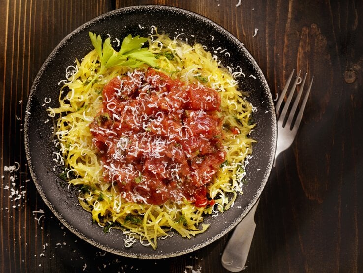 Draufsicht auf einen runden Teller. Darauf angerichtet ist ein gegarter Spaghettikürbis mit Tomatensoße.