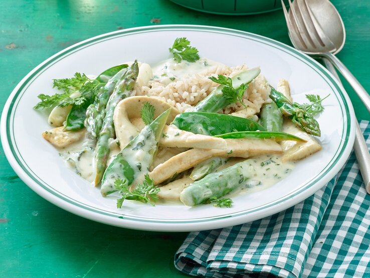 Teller mit Tofu-Geschnetzeltem, grünem Spargel und cremiger Soße.