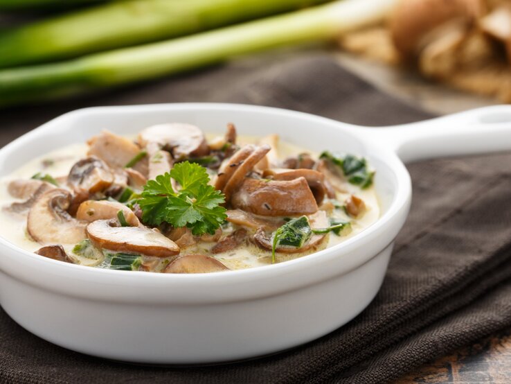 Champignons in Sahnesoße in einer kleinen, weißen Pfanne. 