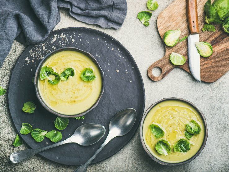 Draufsicht auf eine runde Schüssel gefüllt mit einer cremigen Suppe aus Rosenkohl. Das Ganze steht auf einem runden untersetzer. 