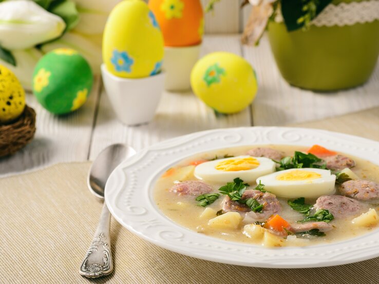 Ein Teller mit der Suppe auf einem hellen Holztisch und Oster-Dekoration. 