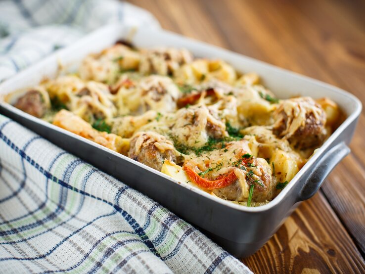 Auflauf mit Kohlrabi und Hackfleisch in einer Auflaufform auf einem Geschirrtuch auf hölzernem Hintergrund. 