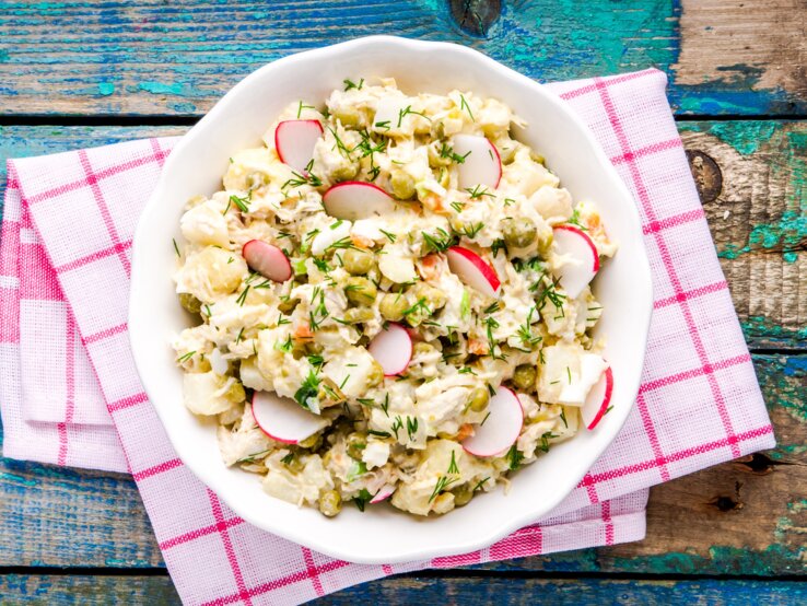 Kohlrabisalat Falscher Kartoffelsalat mit Radieschen und Kräutern in weißer Schale auf rot-weißer Serviette, rustikaler Holztisch.