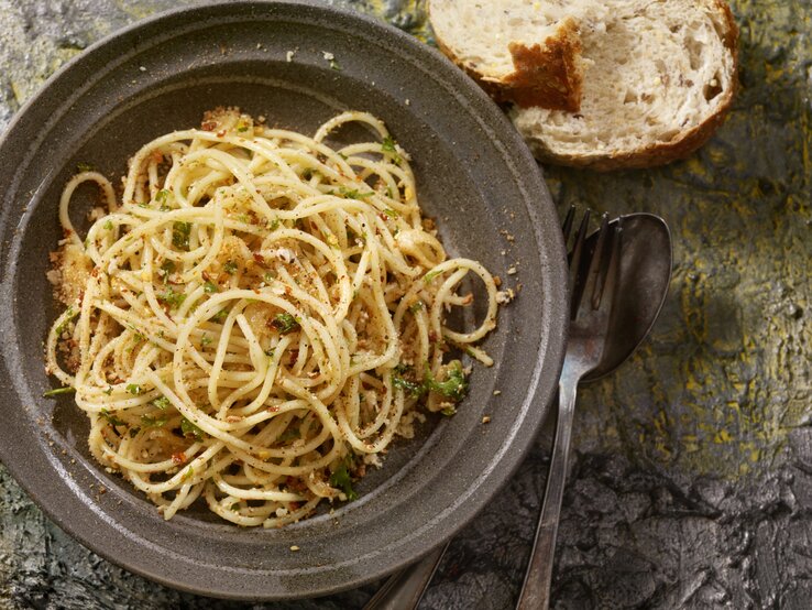 Draufsicht auf einen dunklen Teller befüllt mit Spaghetti Aglio, Olio e Peperoncini. 