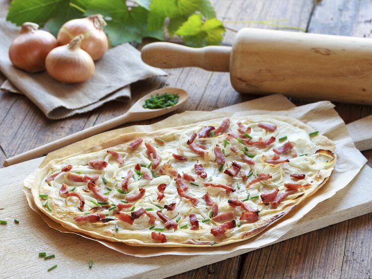 Frisch gebackener Flammkuchen mit Speck auf einem Holzbrett.