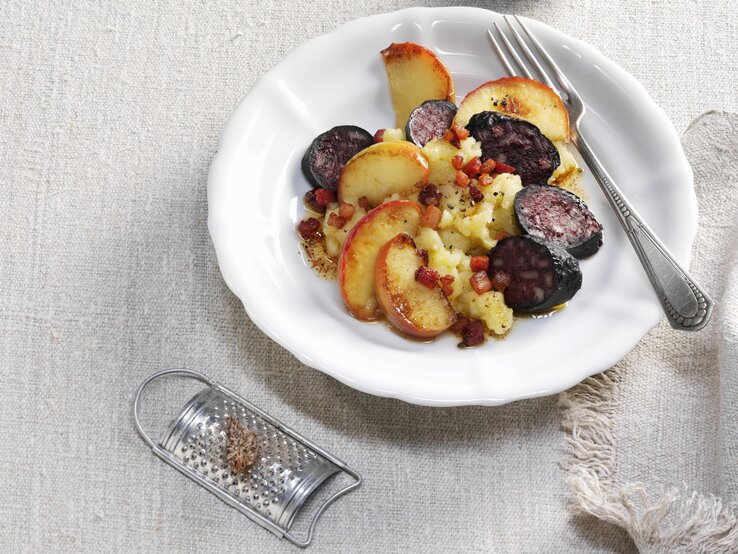 Himmel und Erde mit Kartoffeln, Äpfeln, Speck und Blutwurst / runder Teller / besteck / Nahaufnahme / Draufsicht